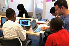 Teacher Mike Mannix meets with students writing on their laptops